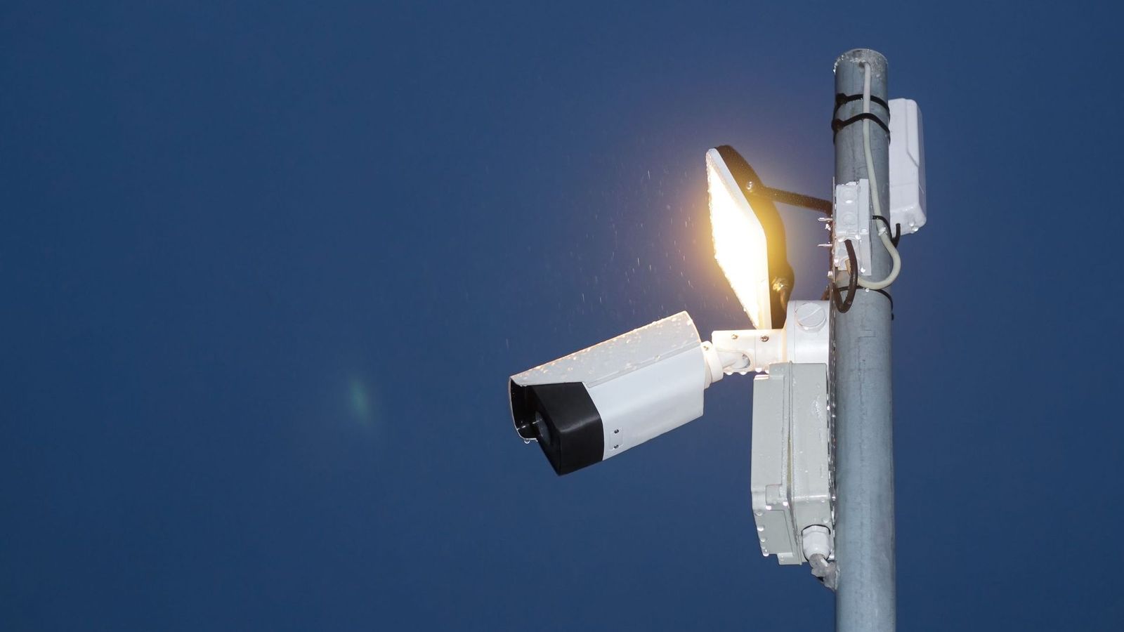 CCTV camera and floodlight on a pole against a night sky