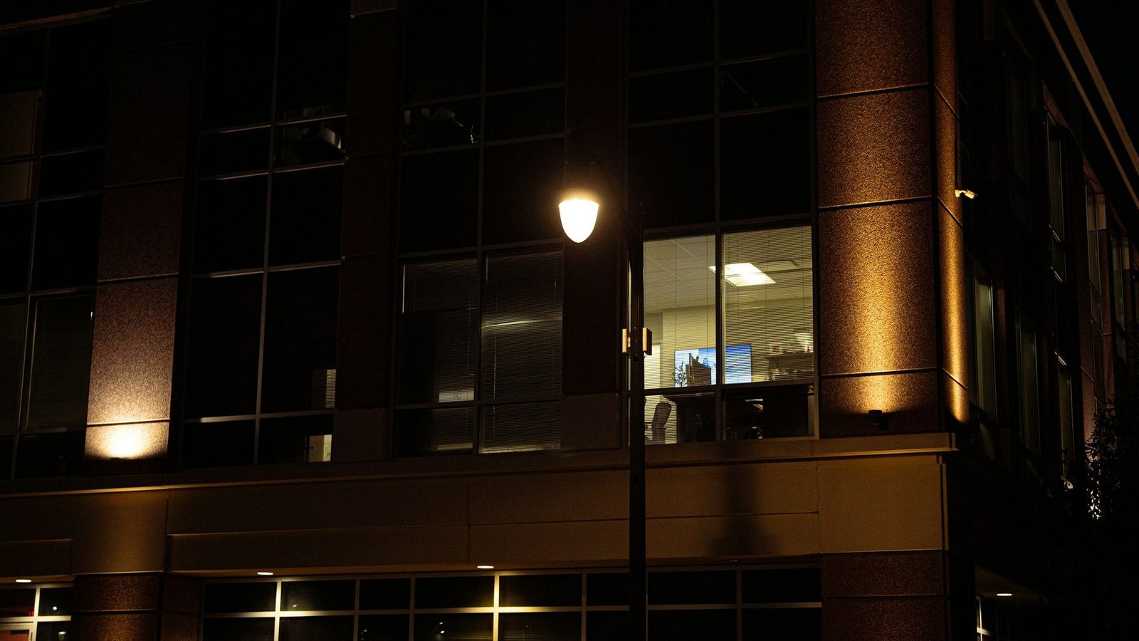 Floodlit office building at night with a CCTV camera on the corner
